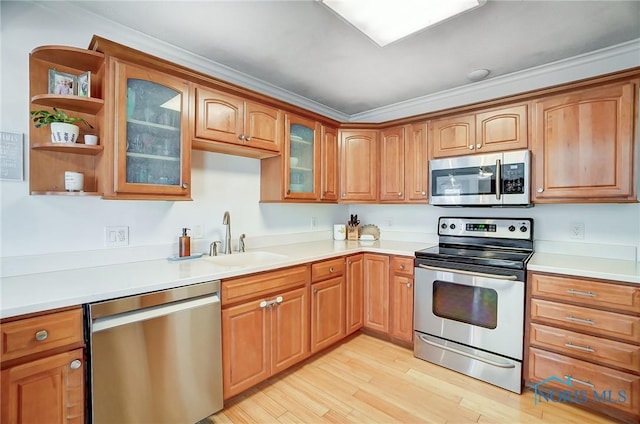 kitchen with light wood-type flooring, appliances with stainless steel finishes, glass insert cabinets, and a sink