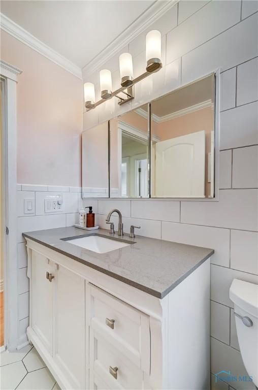 half bath with tile patterned flooring, toilet, vanity, tile walls, and crown molding