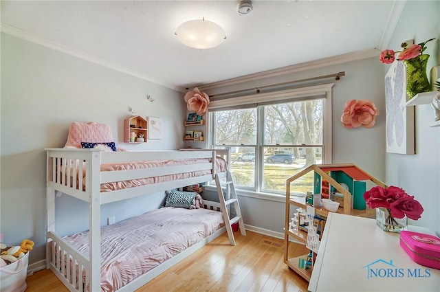 bedroom with ornamental molding, visible vents, baseboards, and wood finished floors