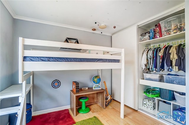 bedroom featuring ornamental molding, a closet, wood finished floors, and baseboards