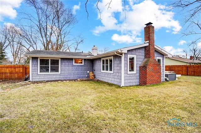 rear view of property with central air condition unit, fence, a chimney, and a lawn