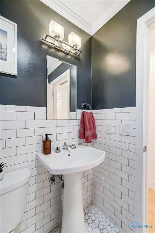 half bath with crown molding, tile walls, and toilet