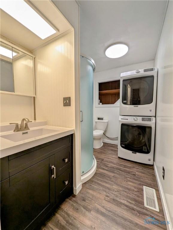 full bathroom featuring a stall shower, visible vents, stacked washer / drying machine, wood finished floors, and vanity