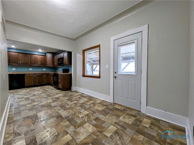 kitchen with dark brown cabinetry, baseboards, stone finish floor, light countertops, and black appliances