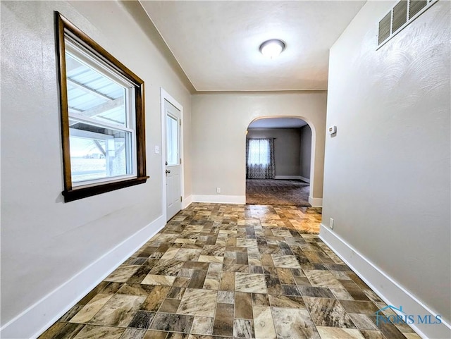 hall with arched walkways, stone finish flooring, visible vents, and baseboards