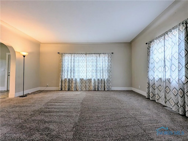 empty room with arched walkways, carpet floors, and baseboards