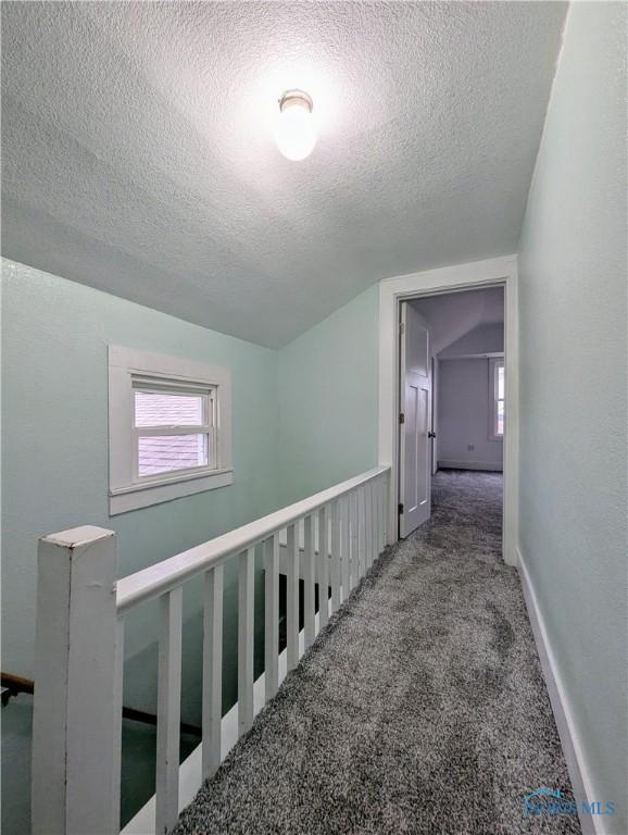 hall featuring a textured ceiling, carpet floors, vaulted ceiling, and an upstairs landing