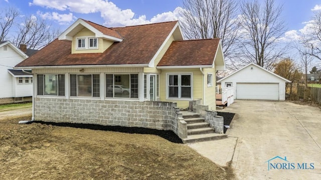 view of front of property featuring a shingled roof, a detached garage, and an outbuilding