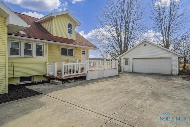 back of house featuring a shingled roof, an outbuilding, a detached garage, and a deck