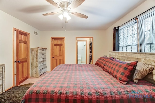 bedroom featuring ensuite bathroom, light carpet, a ceiling fan, visible vents, and a walk in closet