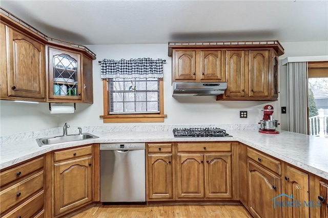 kitchen featuring gas cooktop, under cabinet range hood, a sink, stainless steel dishwasher, and brown cabinets