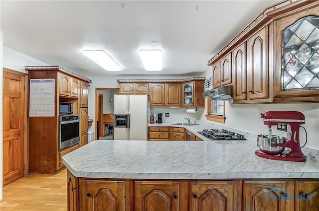 kitchen featuring under cabinet range hood, a peninsula, light countertops, black appliances, and brown cabinetry