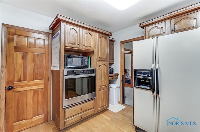 kitchen with black microwave, white fridge with ice dispenser, light wood-style flooring, and oven