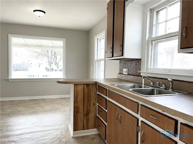 kitchen featuring tasteful backsplash, brown cabinetry, a sink, a peninsula, and baseboards