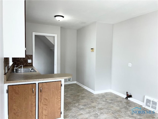 kitchen with visible vents, decorative backsplash, a sink, a peninsula, and baseboards