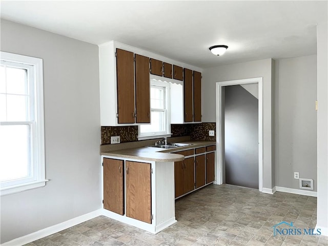 kitchen with a sink, stone finish flooring, baseboards, and backsplash