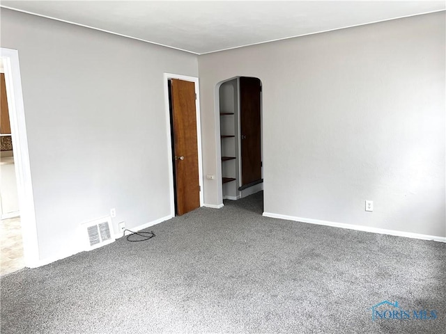 unfurnished room featuring arched walkways, baseboards, visible vents, and carpet flooring