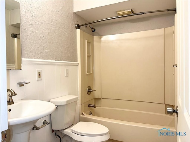 full bath with toilet, a wainscoted wall, a textured wall, and bathing tub / shower combination