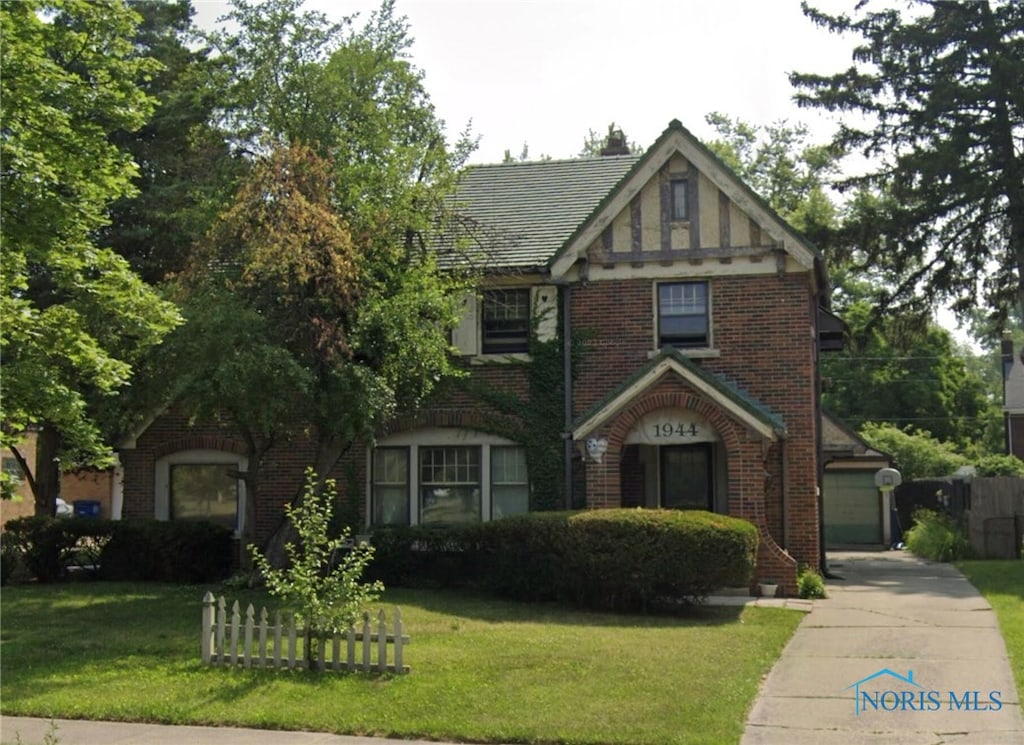 tudor house featuring a garage, a front lawn, and brick siding