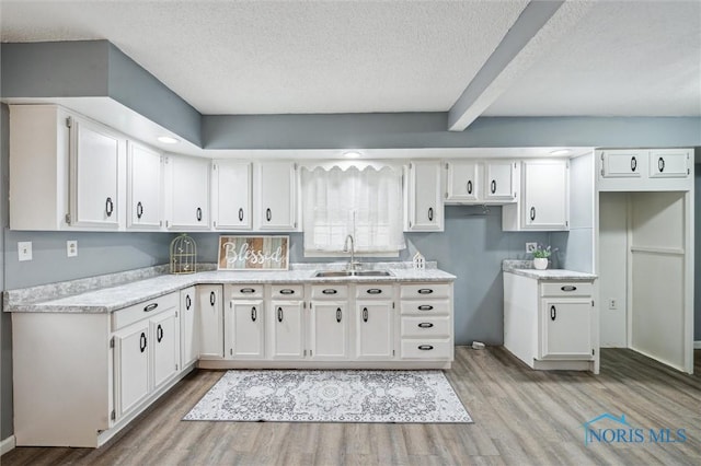 kitchen with a textured ceiling, wood finished floors, a sink, and white cabinets