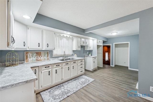 kitchen featuring baseboards, light countertops, light wood-style floors, white cabinetry, and a sink