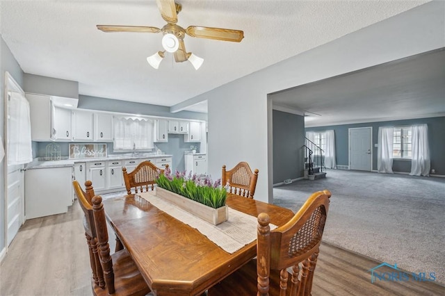 dining area with stairs, a textured ceiling, light carpet, and a ceiling fan