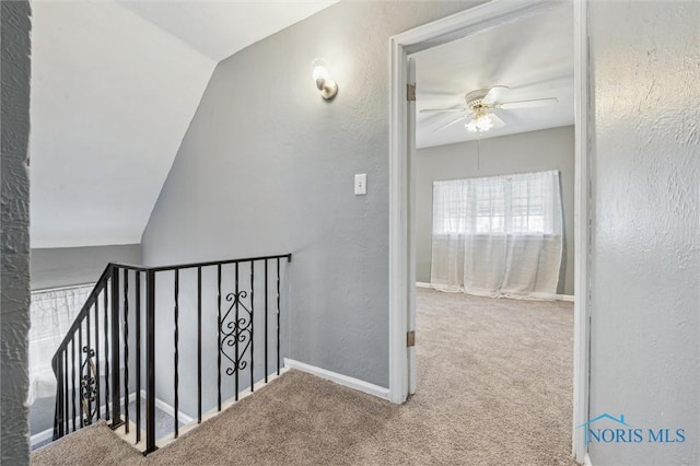 hall with a textured wall, carpet floors, an upstairs landing, and baseboards