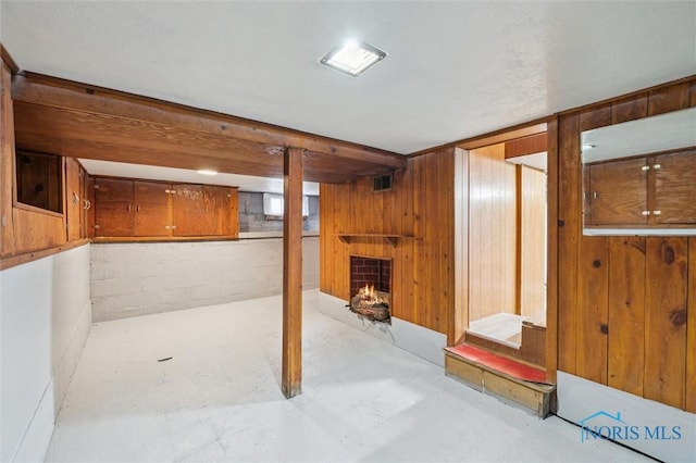 finished basement featuring visible vents, a lit fireplace, wood walls, and concrete block wall