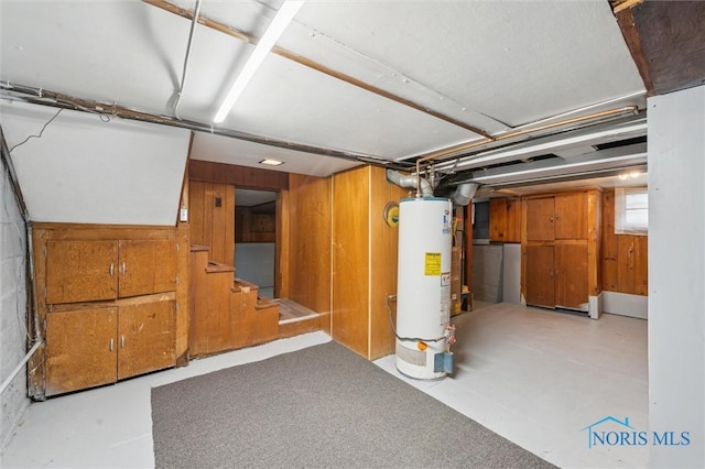 basement featuring gas water heater, wood walls, and stairway