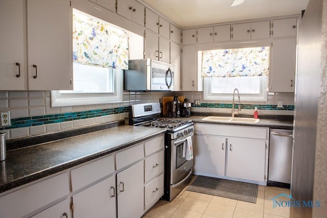 kitchen with stainless steel appliances, a sink, a wealth of natural light, decorative backsplash, and dark countertops