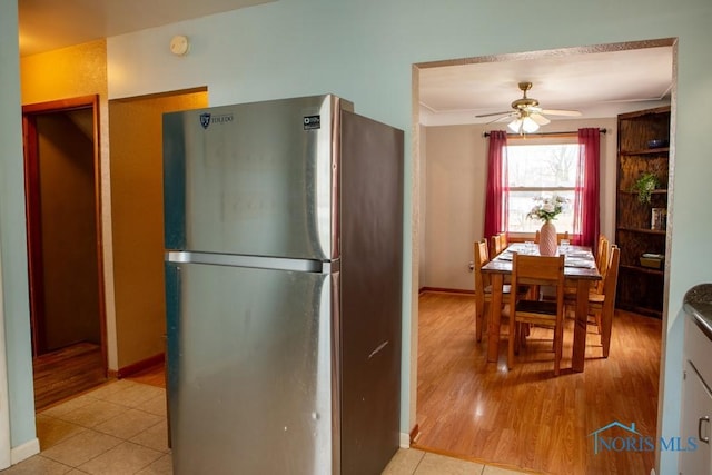 kitchen with light tile patterned floors, baseboards, freestanding refrigerator, and a ceiling fan