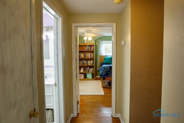 hallway with a textured wall, wood finished floors, and baseboards