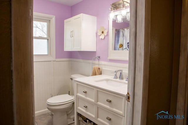 bathroom featuring toilet, tile patterned floors, vanity, wainscoting, and a shower with curtain