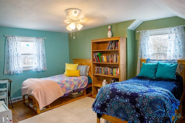 bedroom with lofted ceiling, multiple windows, visible vents, and wood finished floors