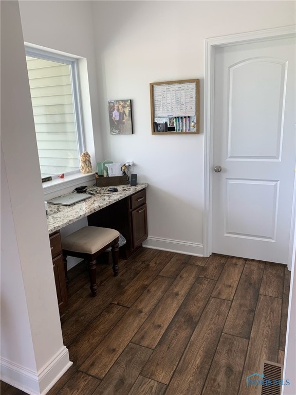 home office featuring dark wood-type flooring, built in desk, and baseboards