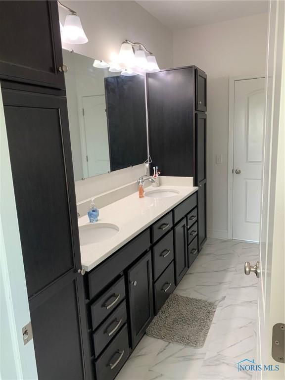 full bath with double vanity, marble finish floor, baseboards, and a sink