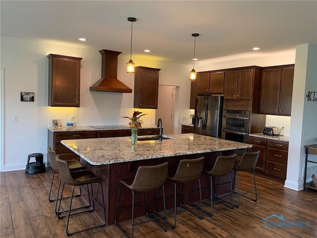 kitchen with dark brown cabinetry, wall chimney exhaust hood, fridge with ice dispenser, double oven, and a sink