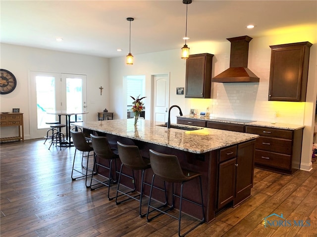 kitchen featuring wall chimney exhaust hood, dark wood-type flooring, a sink, and decorative backsplash