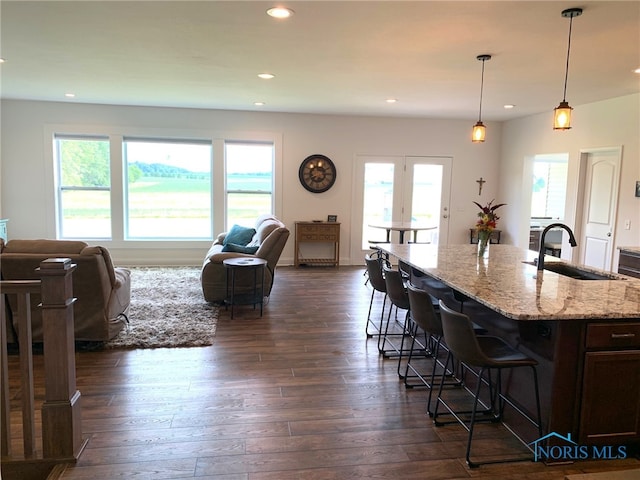 kitchen with a breakfast bar area, dark wood-type flooring, a sink, open floor plan, and light stone countertops