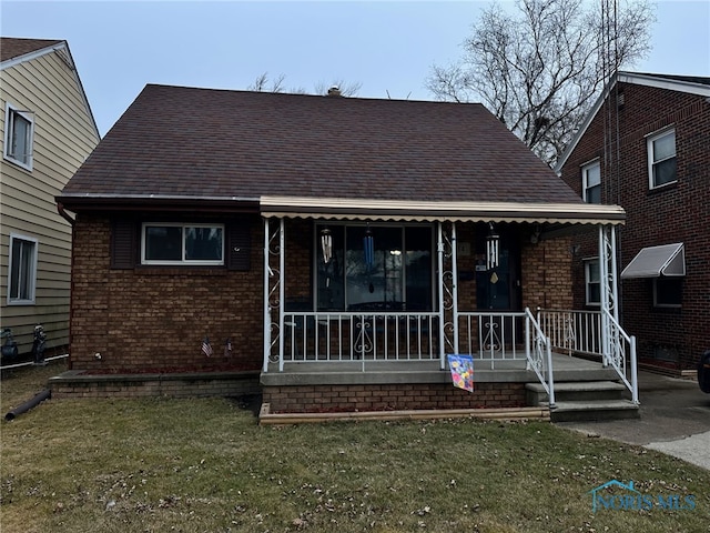 view of front facade with a porch, brick siding, a shingled roof, and a front lawn