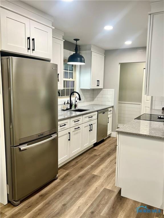 kitchen with decorative backsplash, white cabinets, light wood-type flooring, and stainless steel appliances