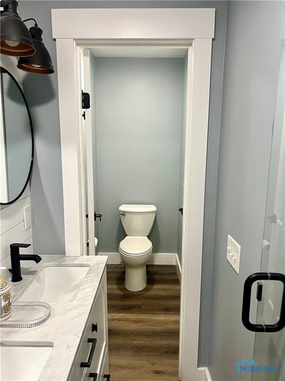 full bath featuring wood finished floors, baseboards, double vanity, a sink, and toilet