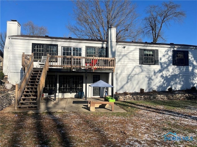 back of house with stairs, a patio, a wooden deck, and a chimney