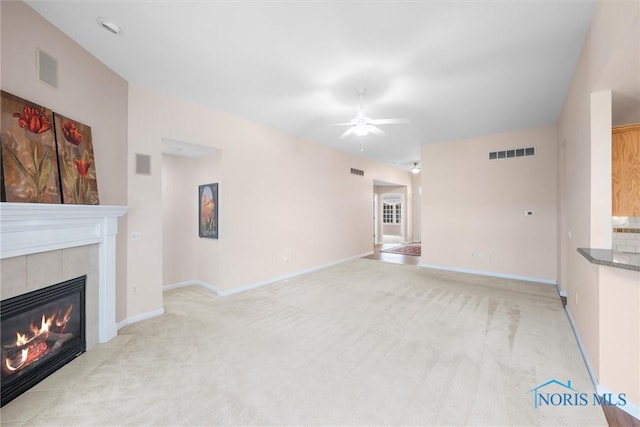 unfurnished living room featuring a ceiling fan, a tile fireplace, visible vents, and light colored carpet