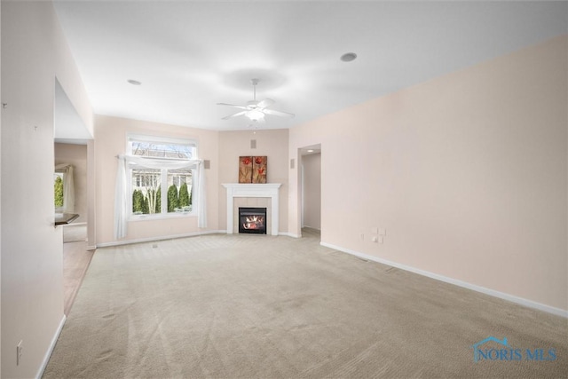 unfurnished living room featuring a ceiling fan, a tile fireplace, baseboards, and carpet