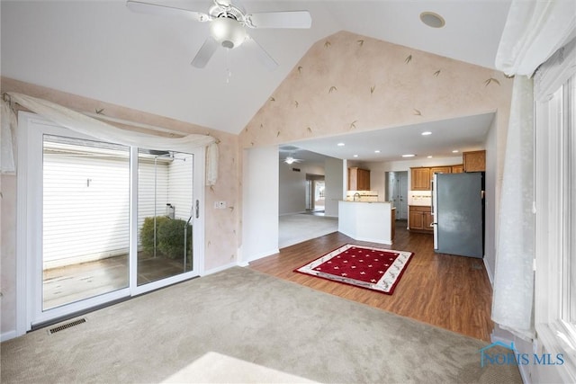 unfurnished living room featuring high vaulted ceiling, dark colored carpet, a wealth of natural light, and visible vents