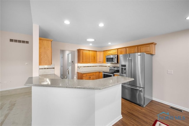 kitchen featuring a peninsula, appliances with stainless steel finishes, a sink, and visible vents