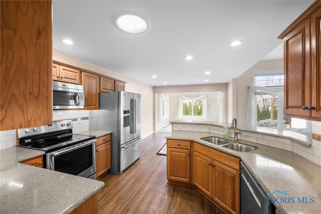 kitchen featuring dark wood-type flooring, a sink, appliances with stainless steel finishes, decorative backsplash, and brown cabinetry