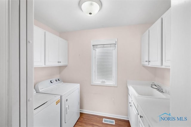 clothes washing area featuring separate washer and dryer, a sink, visible vents, baseboards, and cabinet space