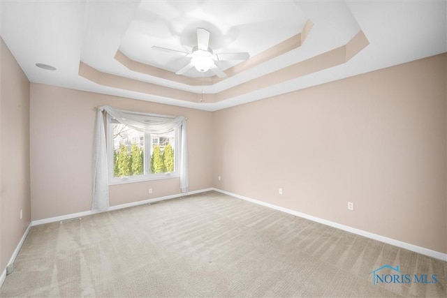 carpeted empty room featuring ceiling fan, a tray ceiling, visible vents, and baseboards